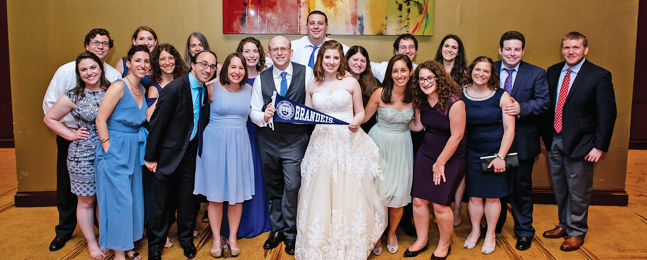 Bride and groom hold a blue Brandeis pennant, with large group of people standing around them